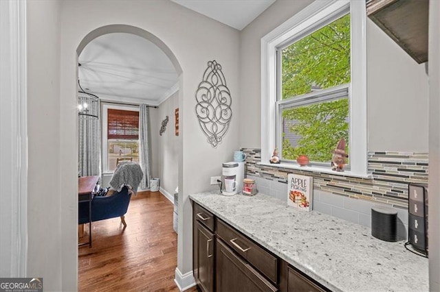 interior space with dark brown cabinetry, light stone countertops, wood-type flooring, and backsplash