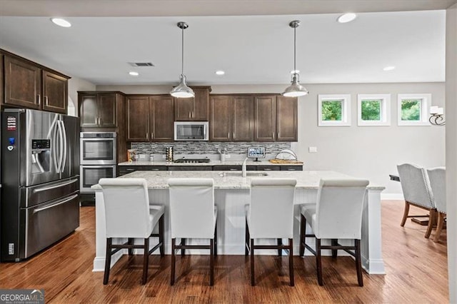 kitchen featuring light stone counters, decorative light fixtures, stainless steel appliances, and an island with sink