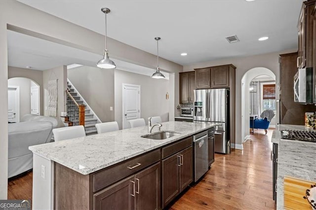 kitchen featuring sink, wood-type flooring, hanging light fixtures, appliances with stainless steel finishes, and a kitchen island with sink