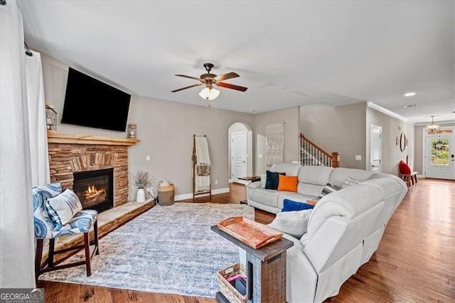 living room featuring ceiling fan, a stone fireplace, and light wood-type flooring