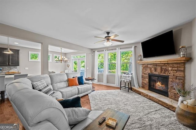 living room featuring ceiling fan with notable chandelier, a stone fireplace, and hardwood / wood-style floors