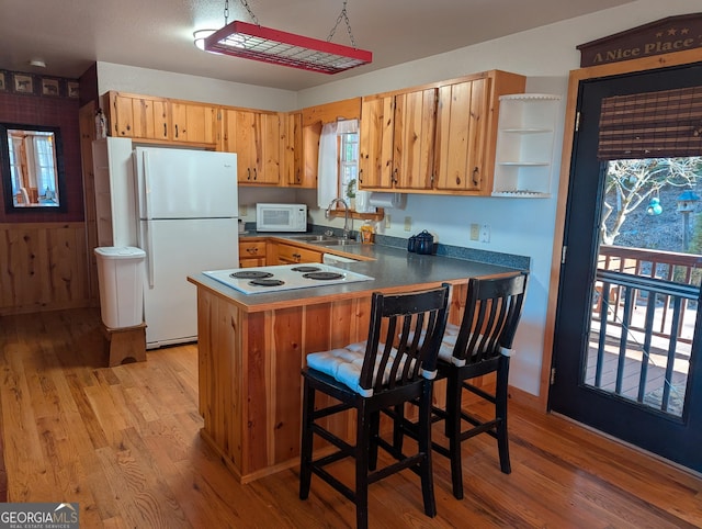 kitchen featuring sink, a breakfast bar area, light wood-type flooring, kitchen peninsula, and white appliances