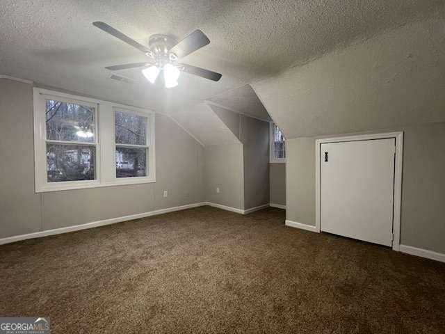 bonus room featuring ceiling fan, lofted ceiling, a textured ceiling, and dark colored carpet