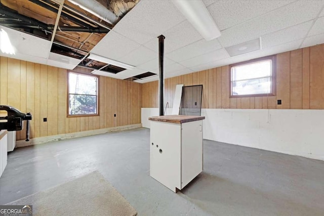 basement featuring wood walls, plenty of natural light, and a drop ceiling