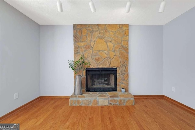 unfurnished living room with wood-type flooring, a stone fireplace, and a textured ceiling