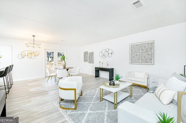 living room with a chandelier, light hardwood / wood-style floors, and french doors