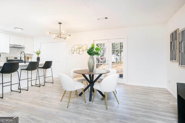 dining space featuring french doors, sink, a chandelier, and light hardwood / wood-style flooring