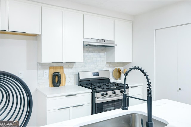 kitchen featuring white cabinetry, stainless steel gas range, light stone counters, and decorative backsplash