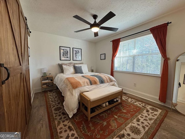 bedroom with ceiling fan, dark wood-type flooring, a barn door, and a textured ceiling