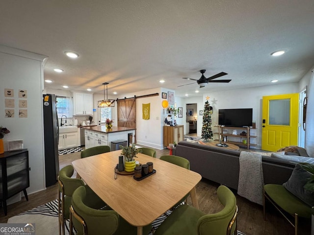 dining room featuring sink, a textured ceiling, dark hardwood / wood-style floors, ceiling fan, and a barn door