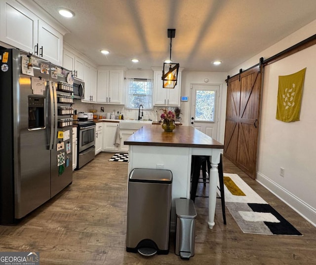 kitchen with dark wood-type flooring, hanging light fixtures, appliances with stainless steel finishes, a barn door, and white cabinets