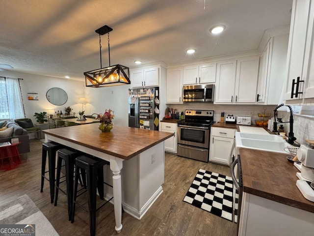 kitchen with butcher block countertops, a breakfast bar area, white cabinetry, stainless steel appliances, and decorative light fixtures