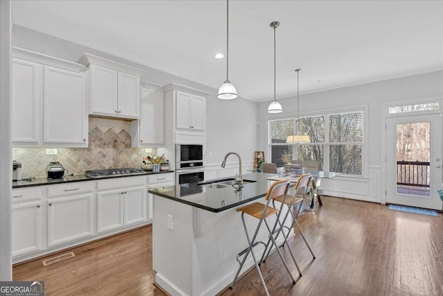 kitchen with sink, appliances with stainless steel finishes, white cabinets, a center island with sink, and decorative light fixtures