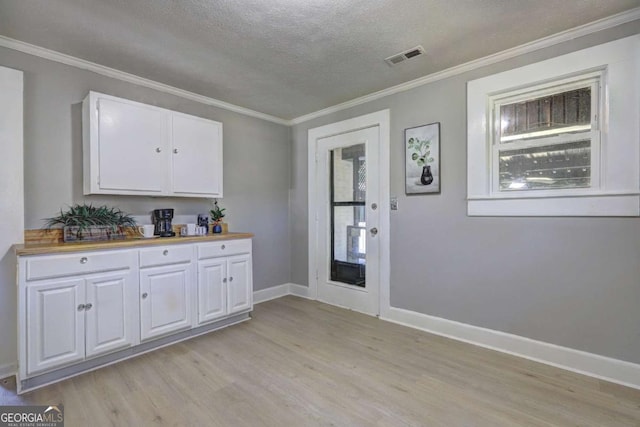 kitchen with white cabinetry, crown molding, light hardwood / wood-style flooring, and a textured ceiling