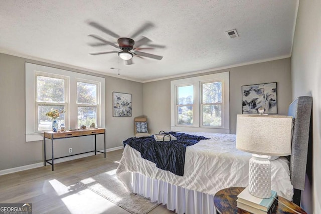 bedroom with ornamental molding, ceiling fan, a textured ceiling, and light wood-type flooring