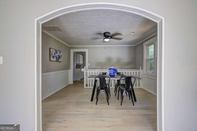 dining space featuring a textured ceiling, ornamental molding, light hardwood / wood-style floors, and ceiling fan