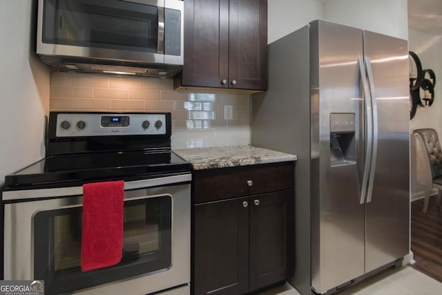 kitchen featuring stainless steel appliances, dark brown cabinets, backsplash, and light stone counters