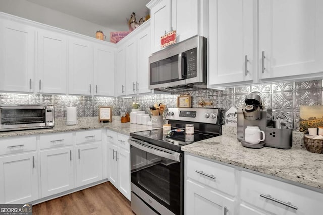 kitchen with light stone counters, dark hardwood / wood-style flooring, white cabinets, stainless steel appliances, and backsplash