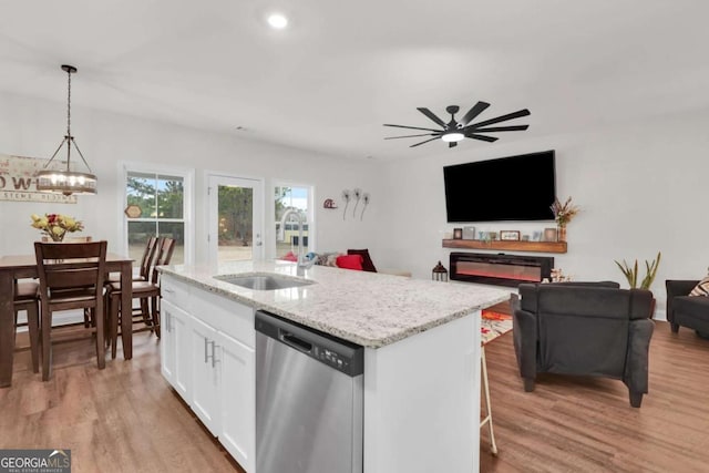 kitchen featuring decorative light fixtures, white cabinetry, an island with sink, stainless steel dishwasher, and light stone counters