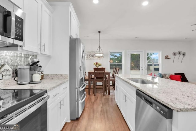 kitchen featuring appliances with stainless steel finishes, white cabinetry, sink, hanging light fixtures, and light stone counters