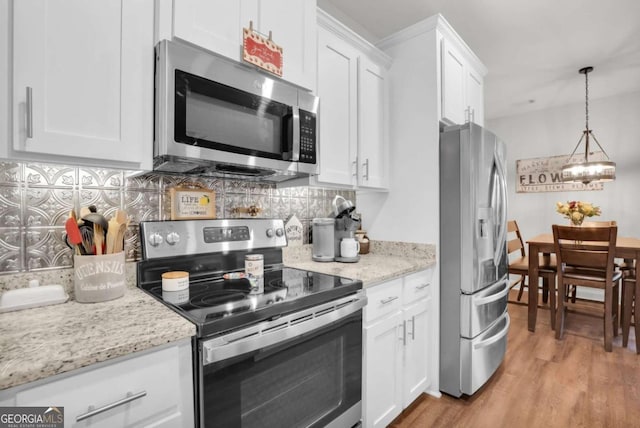 kitchen with pendant lighting, white cabinets, stainless steel appliances, light stone countertops, and light hardwood / wood-style flooring