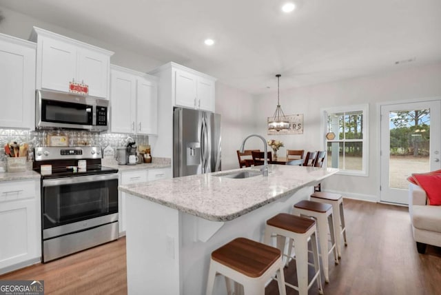 kitchen featuring sink, hanging light fixtures, stainless steel appliances, an island with sink, and white cabinets