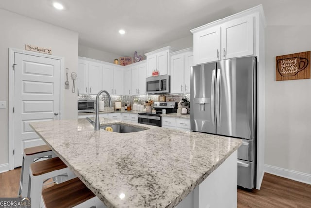 kitchen with sink, a kitchen island with sink, white cabinetry, stainless steel appliances, and light stone countertops