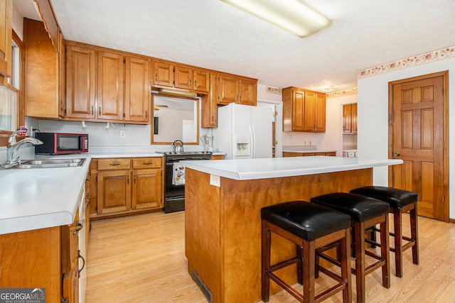 kitchen with a kitchen island, a breakfast bar, sink, white refrigerator with ice dispenser, and black / electric stove