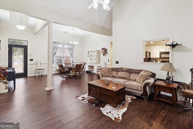 living room featuring dark hardwood / wood-style flooring, a towering ceiling, ceiling fan with notable chandelier, and ornate columns