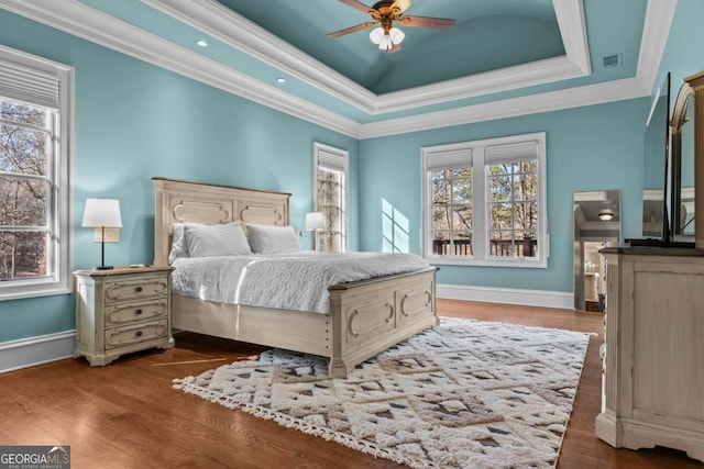 bedroom with crown molding, hardwood / wood-style flooring, a tray ceiling, and ceiling fan