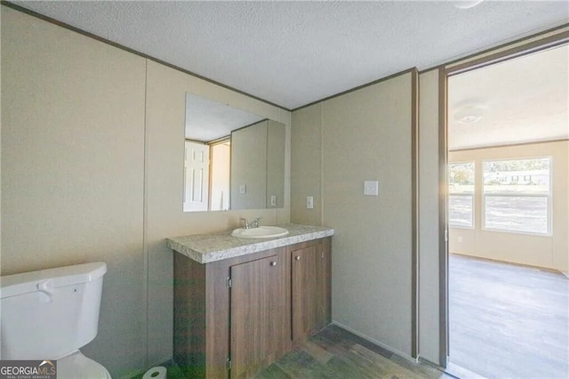 half bath featuring toilet, a textured ceiling, wood finished floors, and vanity