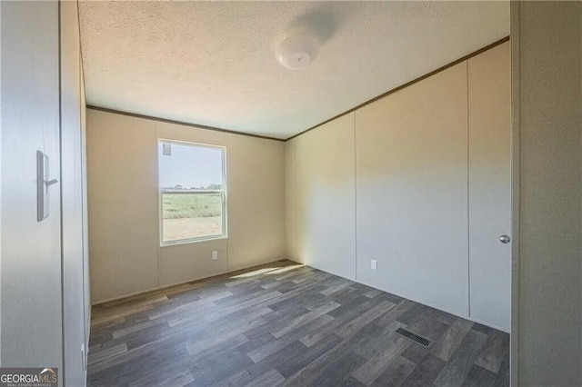 empty room featuring dark wood-style floors, a textured ceiling, visible vents, and crown molding