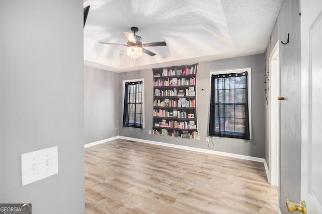 spare room with ceiling fan, a tray ceiling, a textured ceiling, and light hardwood / wood-style flooring