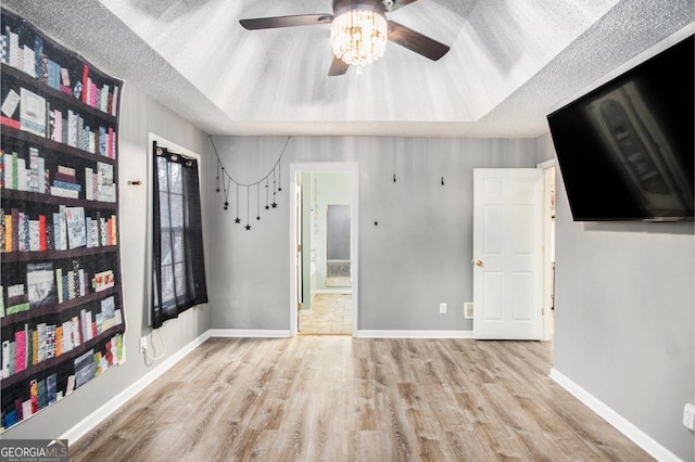 interior space featuring ceiling fan, light hardwood / wood-style floors, a raised ceiling, and a textured ceiling