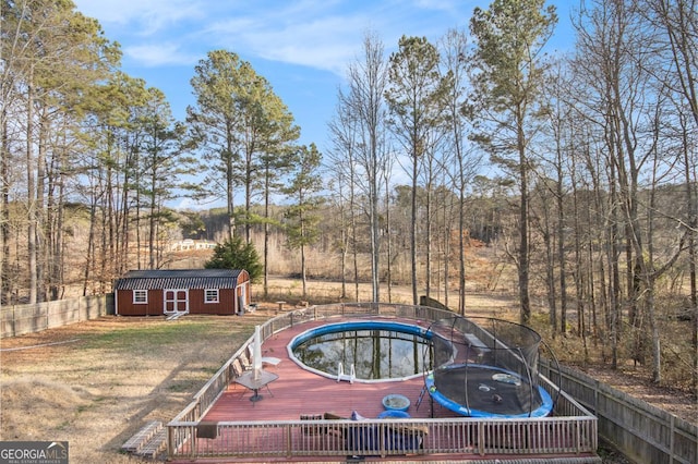 view of swimming pool featuring a trampoline, a storage shed, a lawn, and a wooden deck