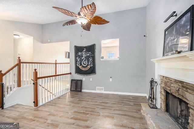 living room with ceiling fan, a textured ceiling, a fireplace, and light wood-type flooring