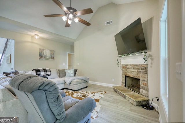 living room featuring ceiling fan, high vaulted ceiling, a stone fireplace, and light hardwood / wood-style floors