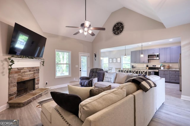 living room featuring ceiling fan, a stone fireplace, high vaulted ceiling, and light wood-type flooring