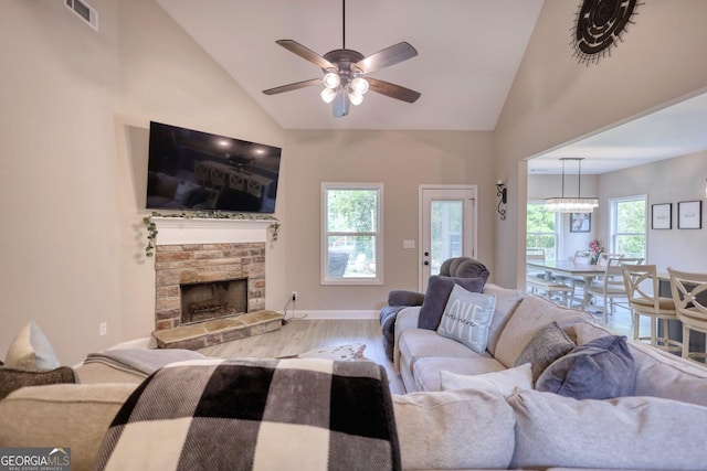 living room with hardwood / wood-style flooring, ceiling fan, a stone fireplace, and high vaulted ceiling