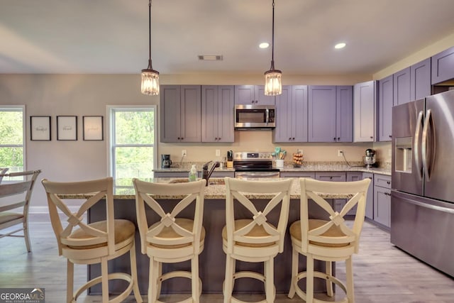 kitchen featuring appliances with stainless steel finishes, decorative light fixtures, light stone countertops, and a wealth of natural light