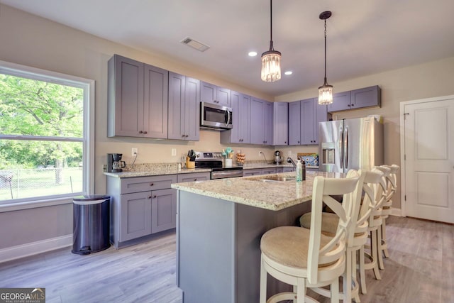 kitchen with sink, a kitchen breakfast bar, stainless steel appliances, light stone countertops, and a kitchen island with sink