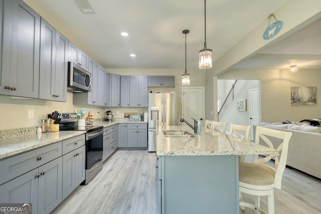 kitchen with pendant lighting, sink, gray cabinets, appliances with stainless steel finishes, and a kitchen bar