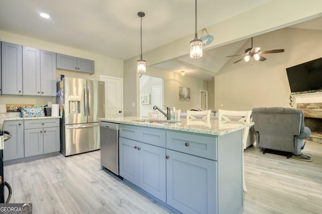 kitchen with decorative light fixtures, an island with sink, sink, stainless steel appliances, and light stone countertops