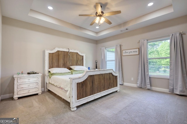 carpeted bedroom featuring ceiling fan, a raised ceiling, and multiple windows