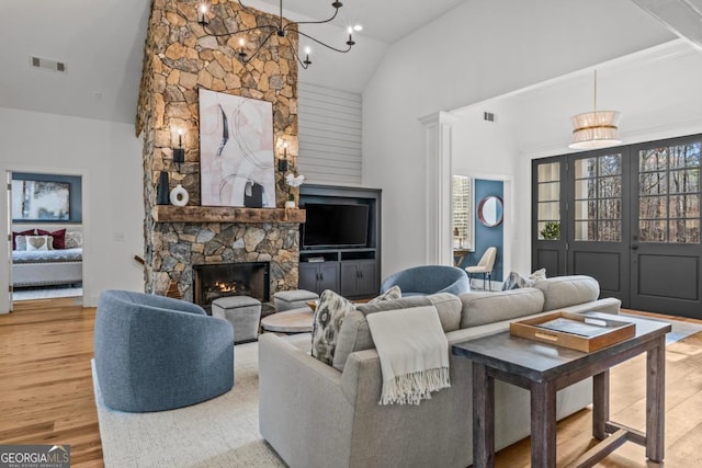 living room featuring an inviting chandelier, hardwood / wood-style flooring, a stone fireplace, and high vaulted ceiling