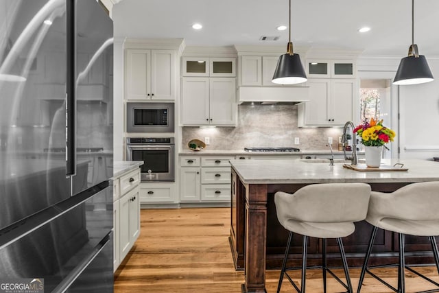 kitchen with pendant lighting, sink, white cabinets, a kitchen island with sink, and stainless steel appliances