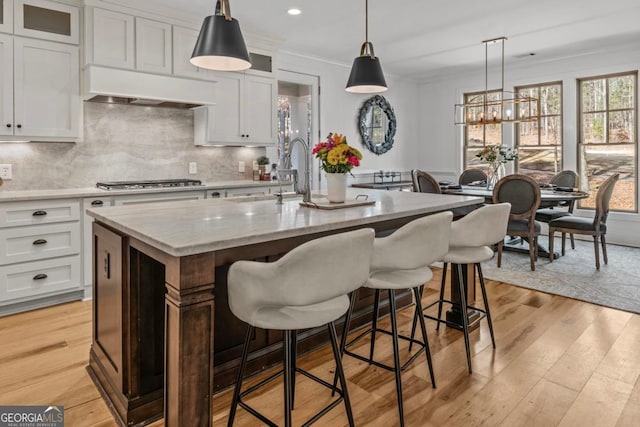 kitchen featuring white cabinetry, a kitchen island with sink, a kitchen breakfast bar, and range hood