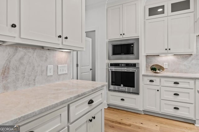 kitchen with built in microwave, white cabinetry, light hardwood / wood-style flooring, oven, and decorative backsplash