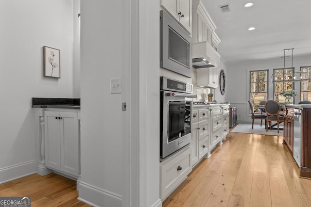 kitchen featuring white cabinetry, stainless steel appliances, hanging light fixtures, and light hardwood / wood-style flooring