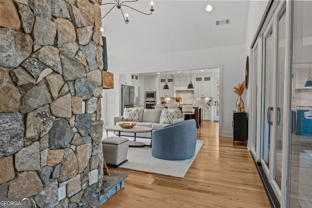 living room with a towering ceiling, an inviting chandelier, and light hardwood / wood-style floors